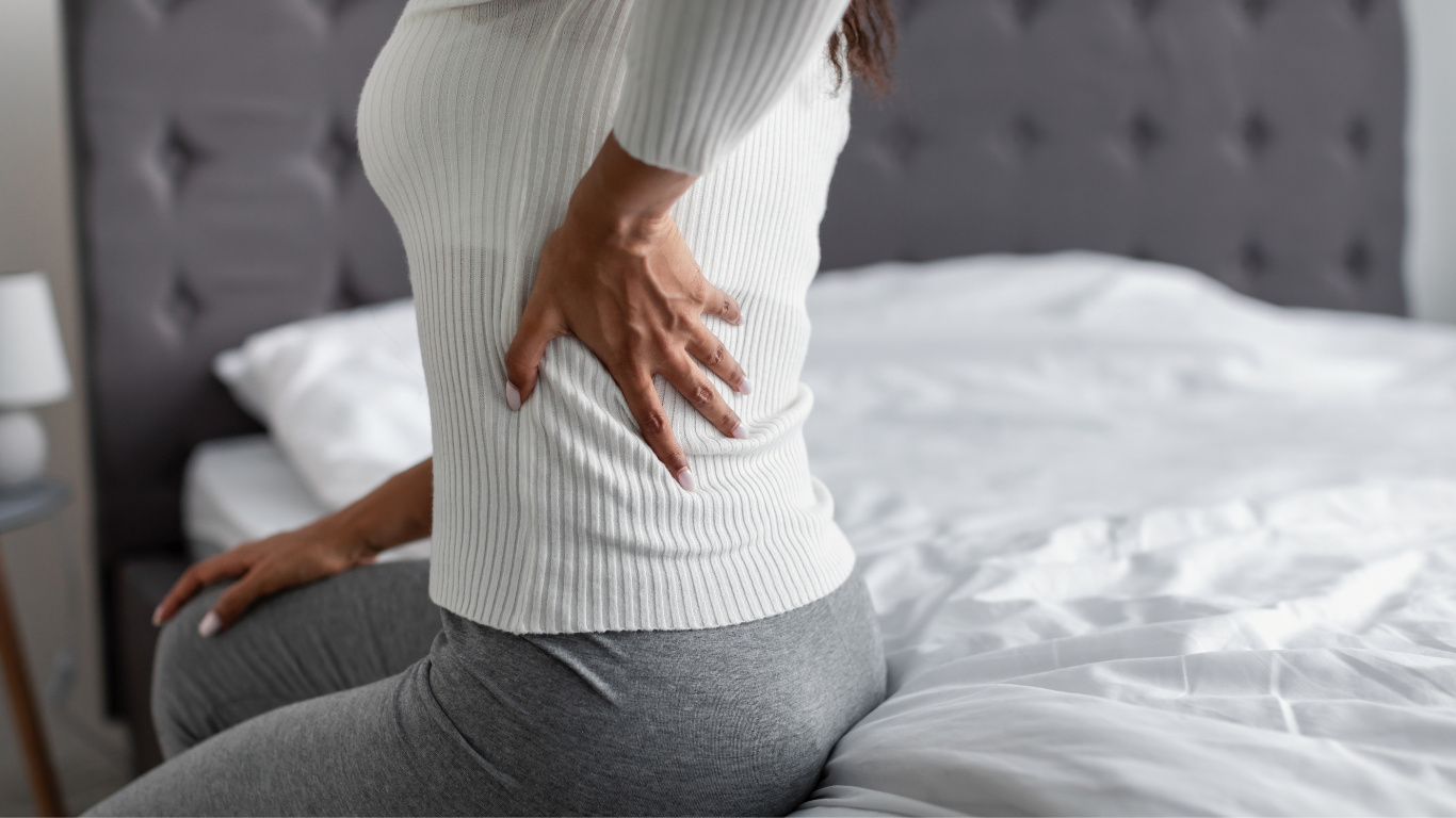 Frau, die am Bett sitzt und sich am Rücken greift