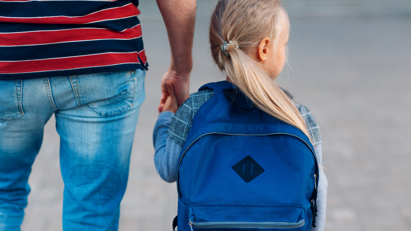 Mann nimmt Kind an der Hand mit Schultasche